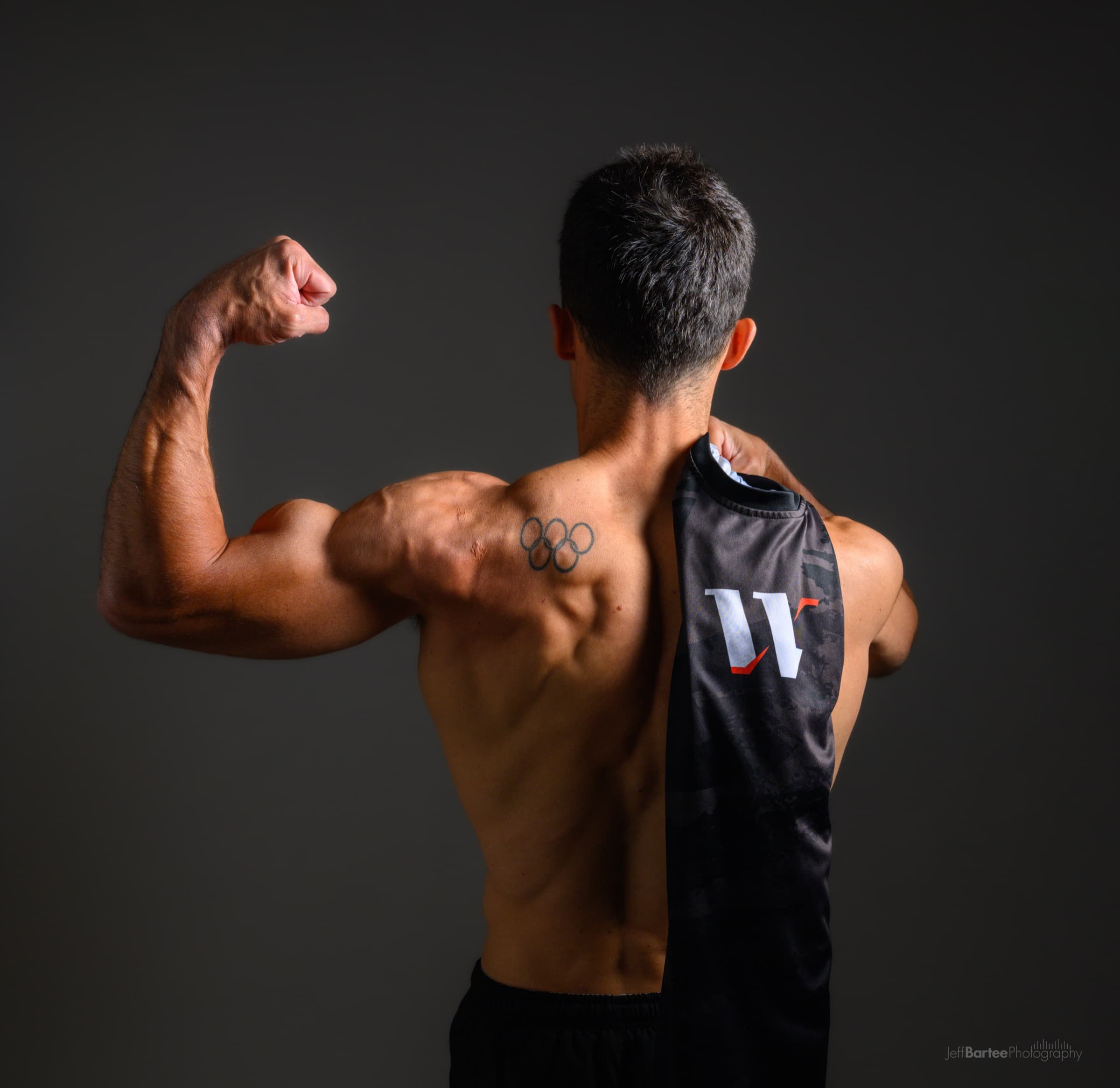 Rubén López flexing, his Olympic rings tattoo visible, holding a WarmApp jersey